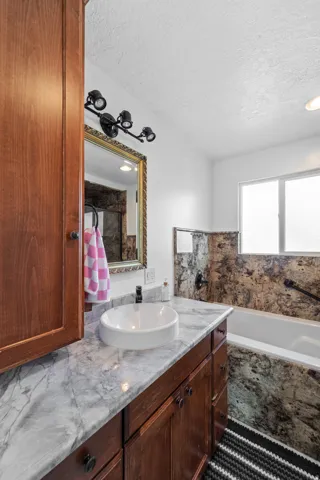 Wood-finish cabinetry with a white vessel sink, patterned countertop, and decorative mirror