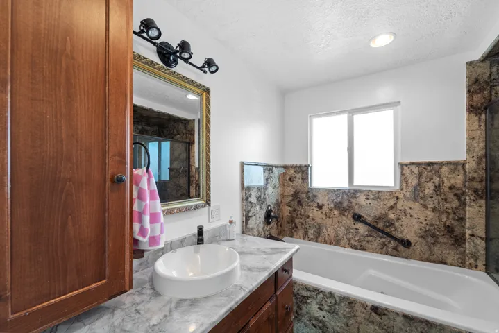 White drop-in bathtub with a grab bar, set against natural stone-look wall panels