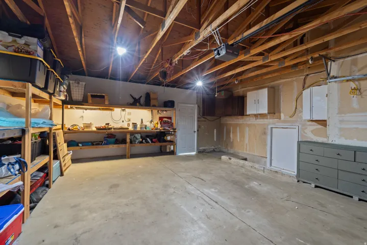 Exposed wood ceiling beams, concrete flooring, built-in shelving, mounted wall cabinets, and a workbench with integrated lighting