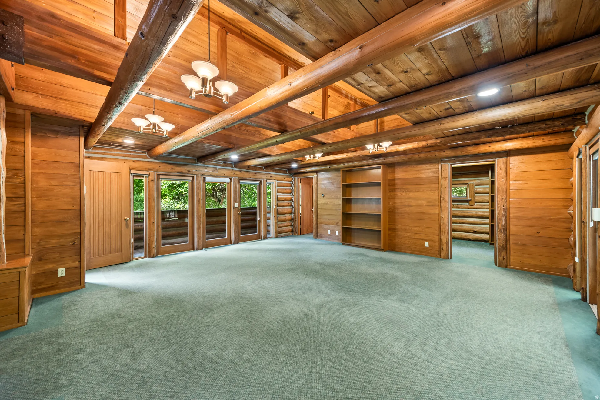 Expansive room featuring exposed log beams, wood-planked walls, built-in shelving, recessed lighting, and multiple doors with glass panels