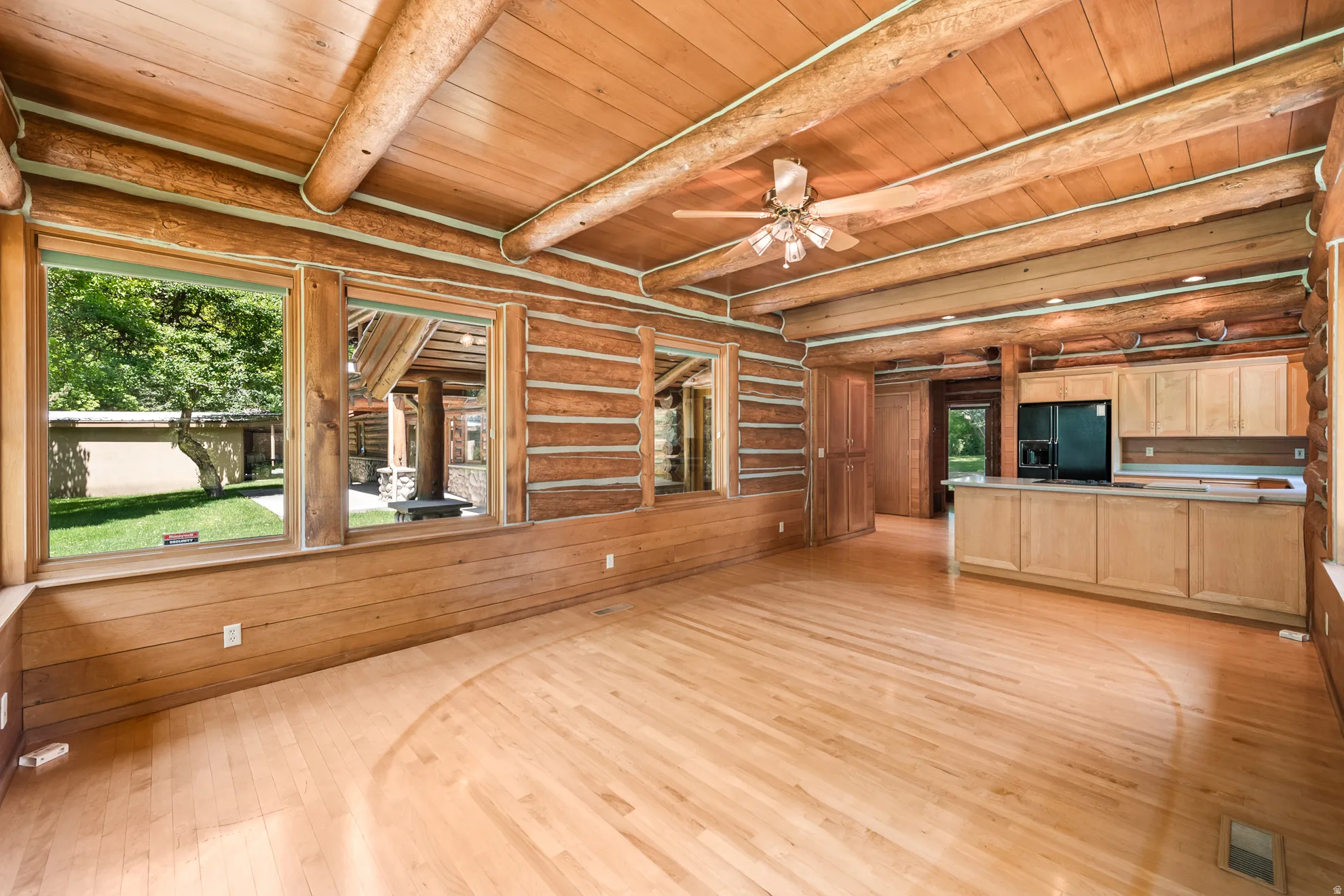 Spacious room featuring exposed log walls, natural wood-finish flooring, and a coordinating wood-paneled ceiling with exposed beams