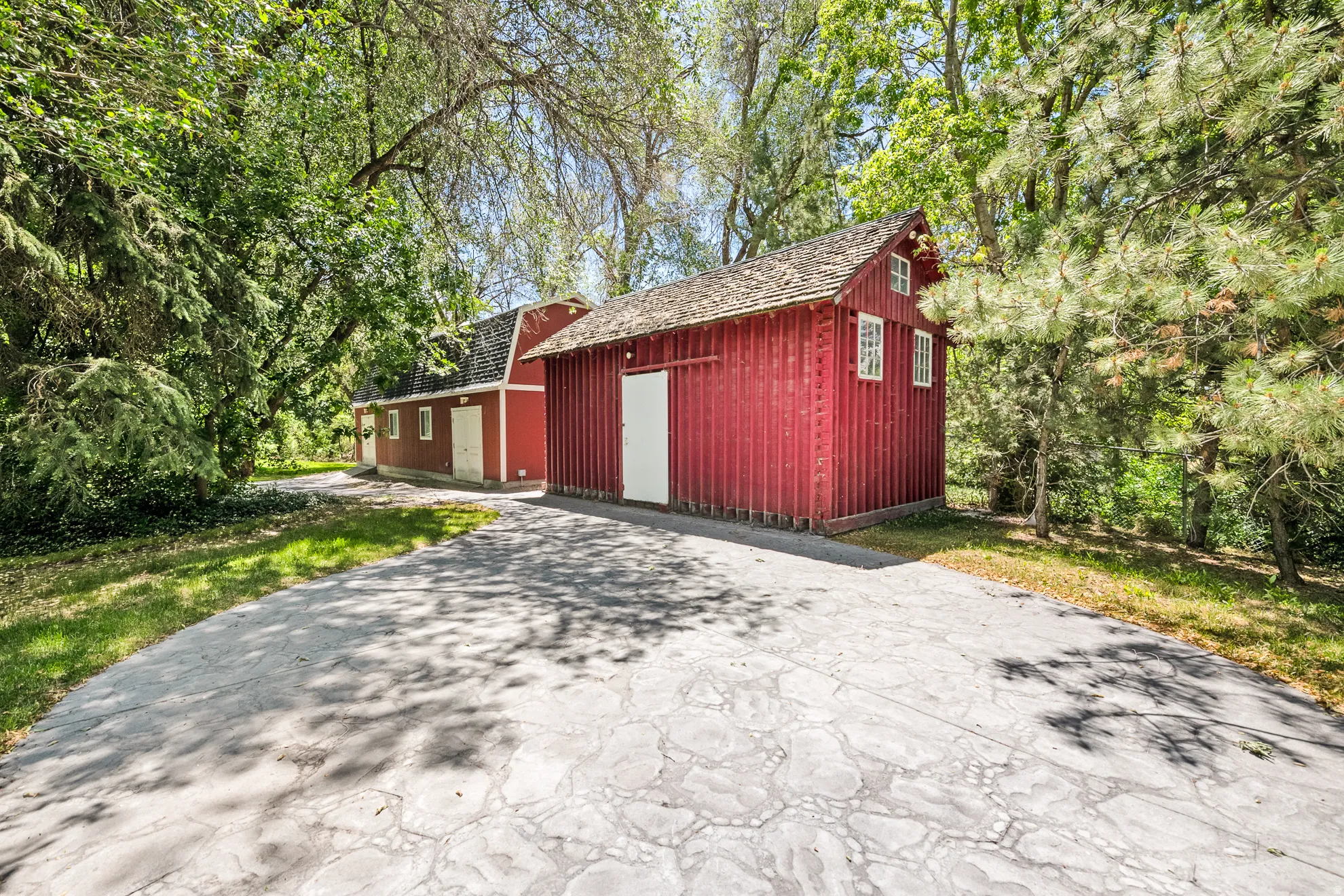 Red-sided detached barn structure featuring a gabled roof with wood shake shingles, white trim windows, and a white barn door