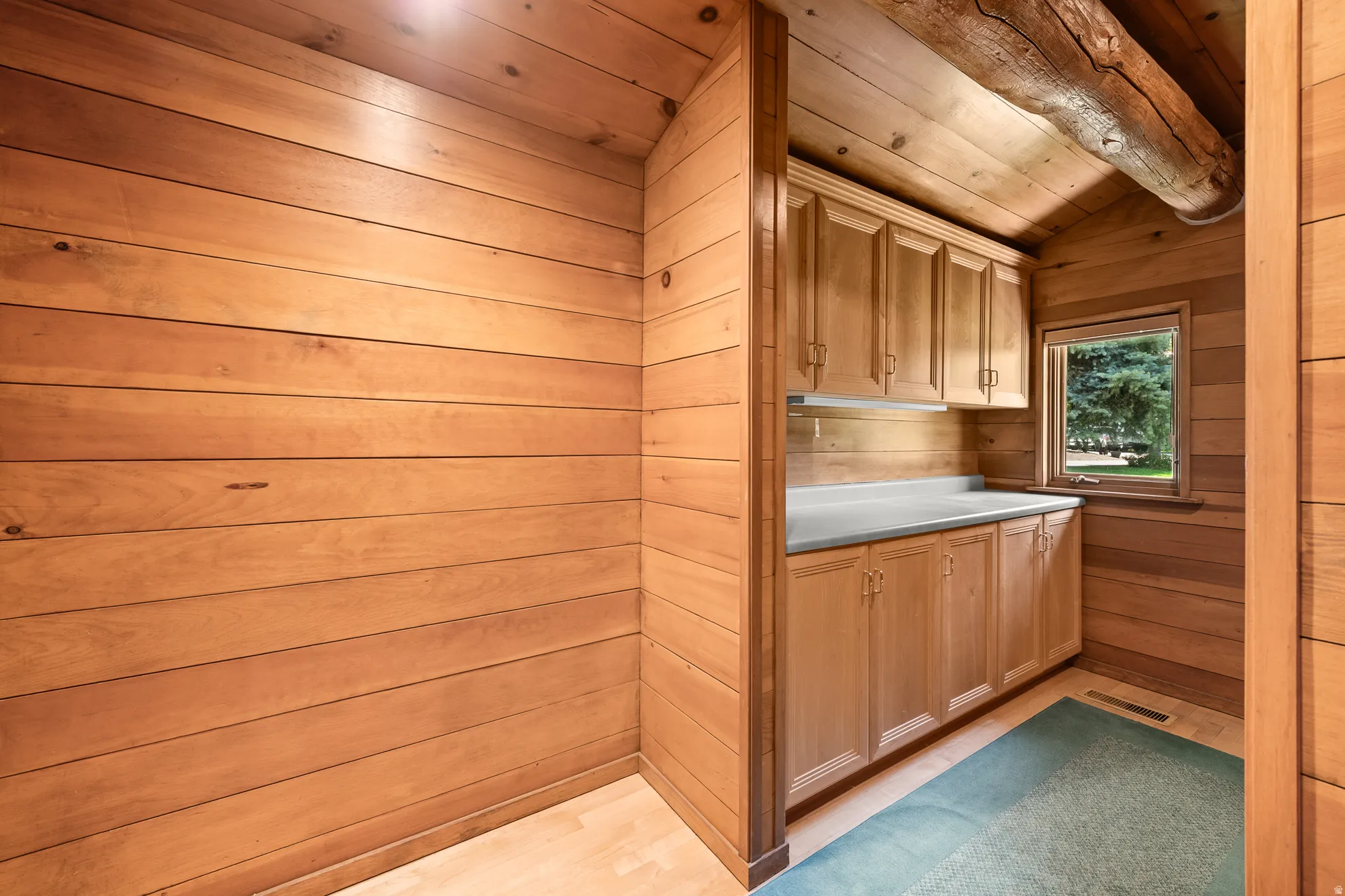 Wood-paneled room featuring custom wood cabinetry with a light-toned countertop, a window with exterior views, and an exposed wood beam ceiling
