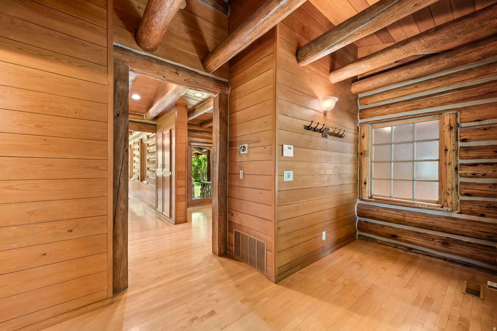 Interior hallway featuring light wood-finish flooring, natural wood plank walls, and exposed log beams