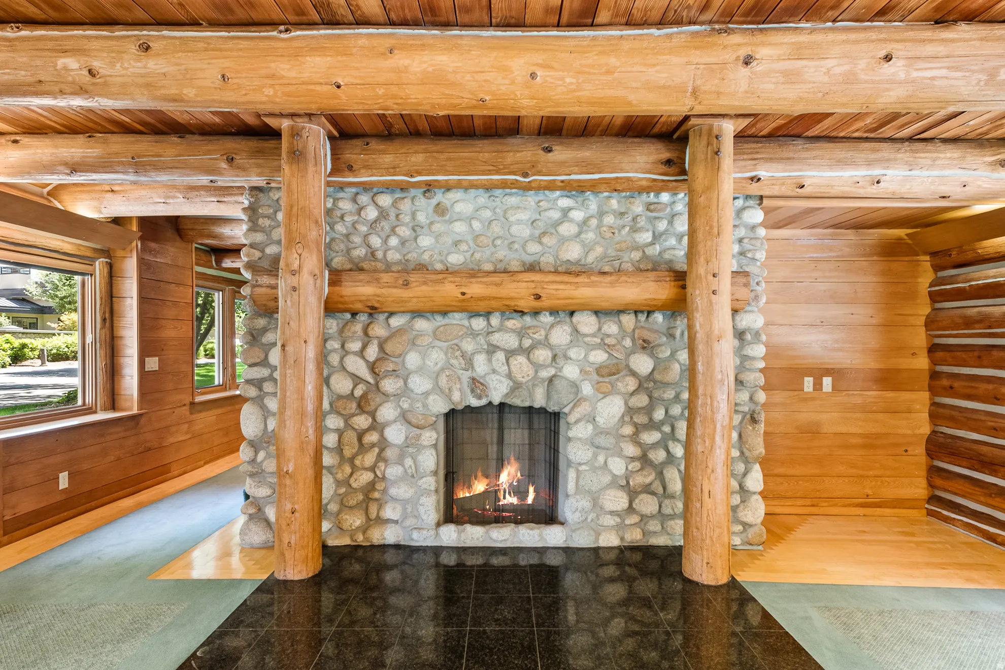 Stone-clad fireplace with a dark tile hearth, framed by exposed log beams and posts