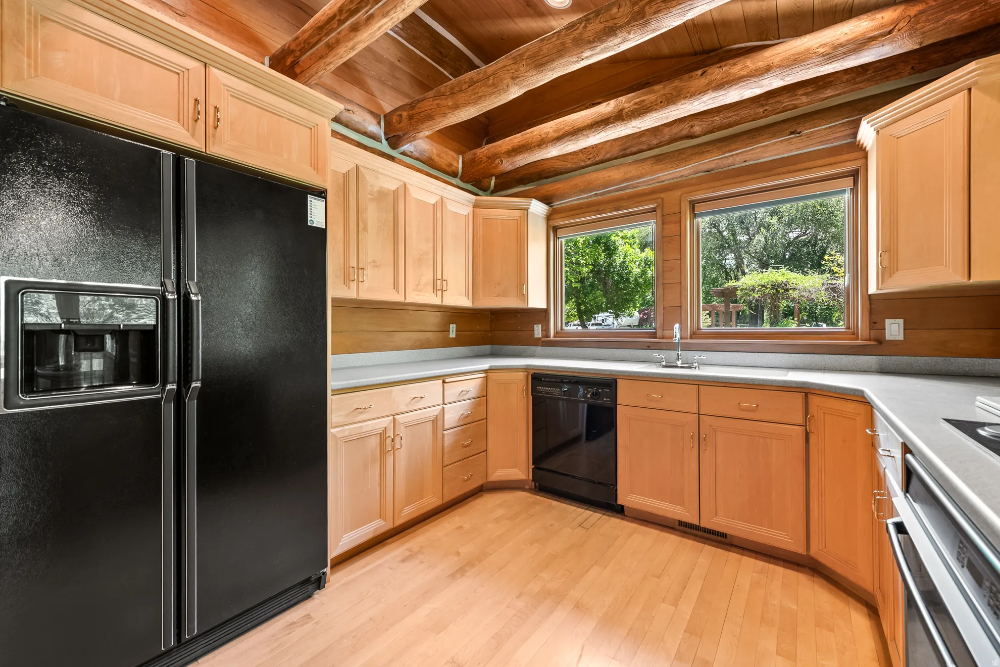 Kitchen featuring light wood cabinetry, wood-finish flooring, and exposed log ceiling beams