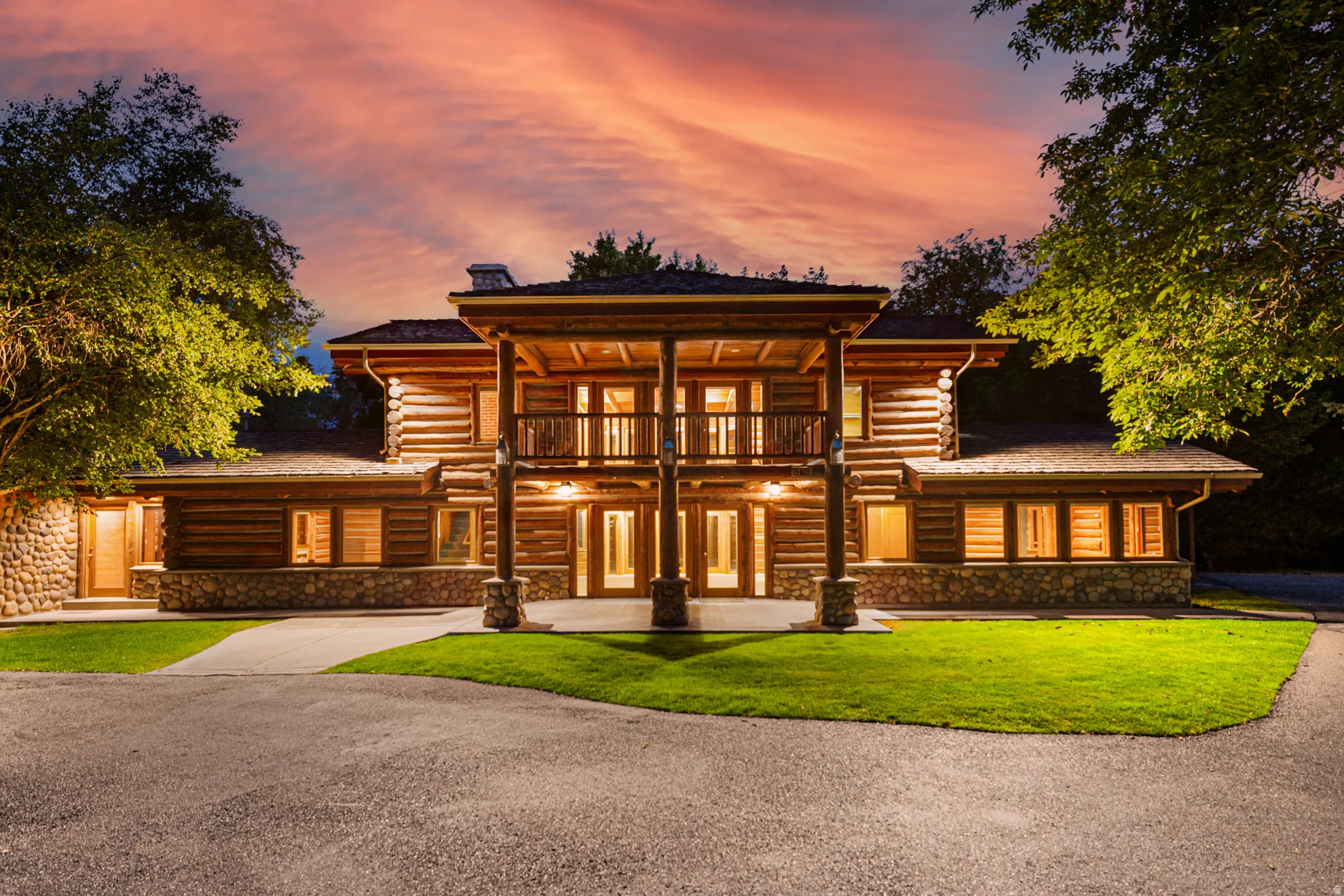 Log home construction featuring stone accents, a covered entry, an upper-level balcony, and a paved driveway