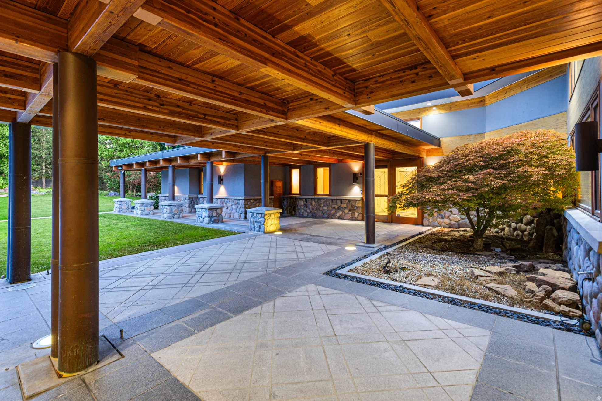 Expansive covered patio with exposed wood ceiling beams, stone accents, and an integrated rock garden