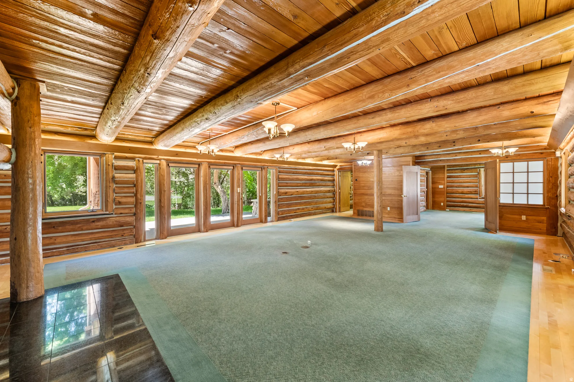 Spacious room featuring exposed log walls, a beamed ceiling, light wood-finish flooring, multiple windows, and recessed lighting fixtures