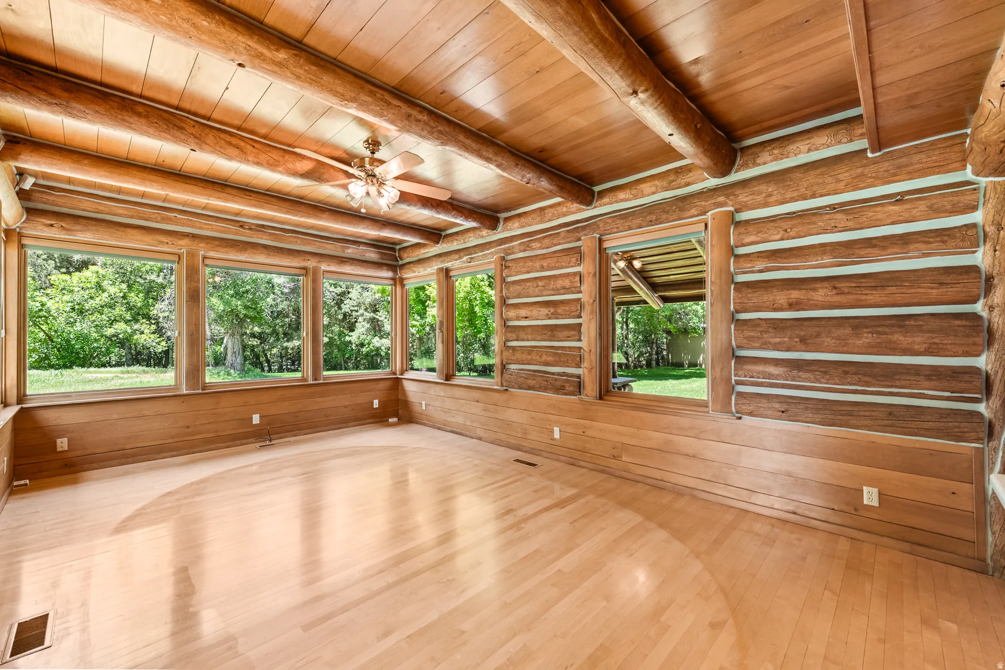Sun-filled room featuring exposed log walls, wood-finish flooring, a wood plank ceiling with exposed beams, and multiple picture windows