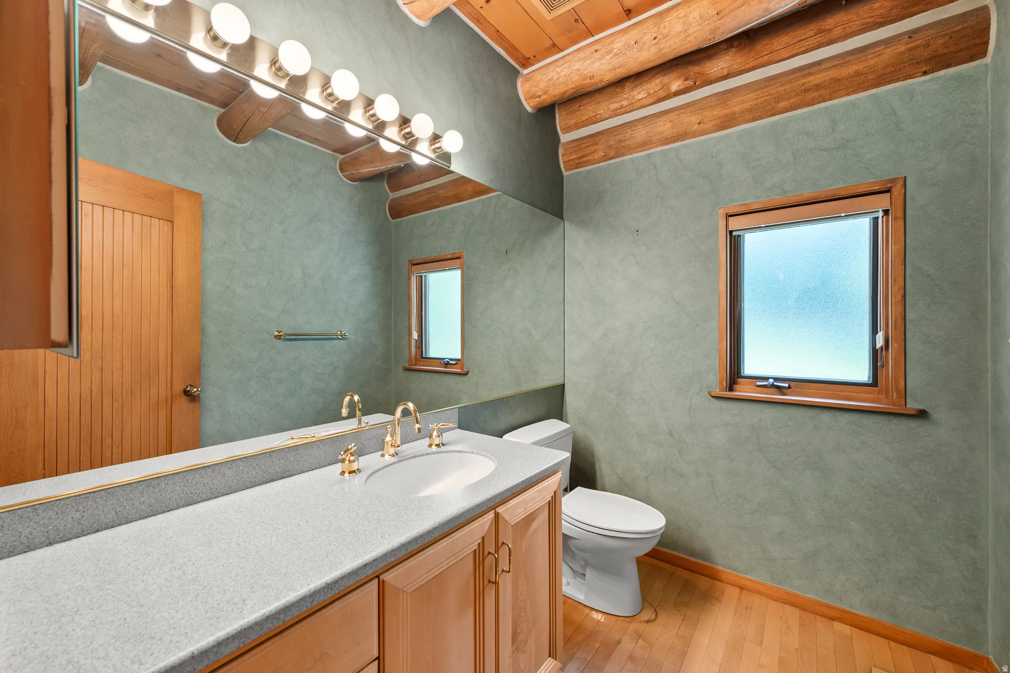 Bathroom featuring a dual-sink vanity with light-colored countertops, gold-finish fixtures, and natural wood cabinetry