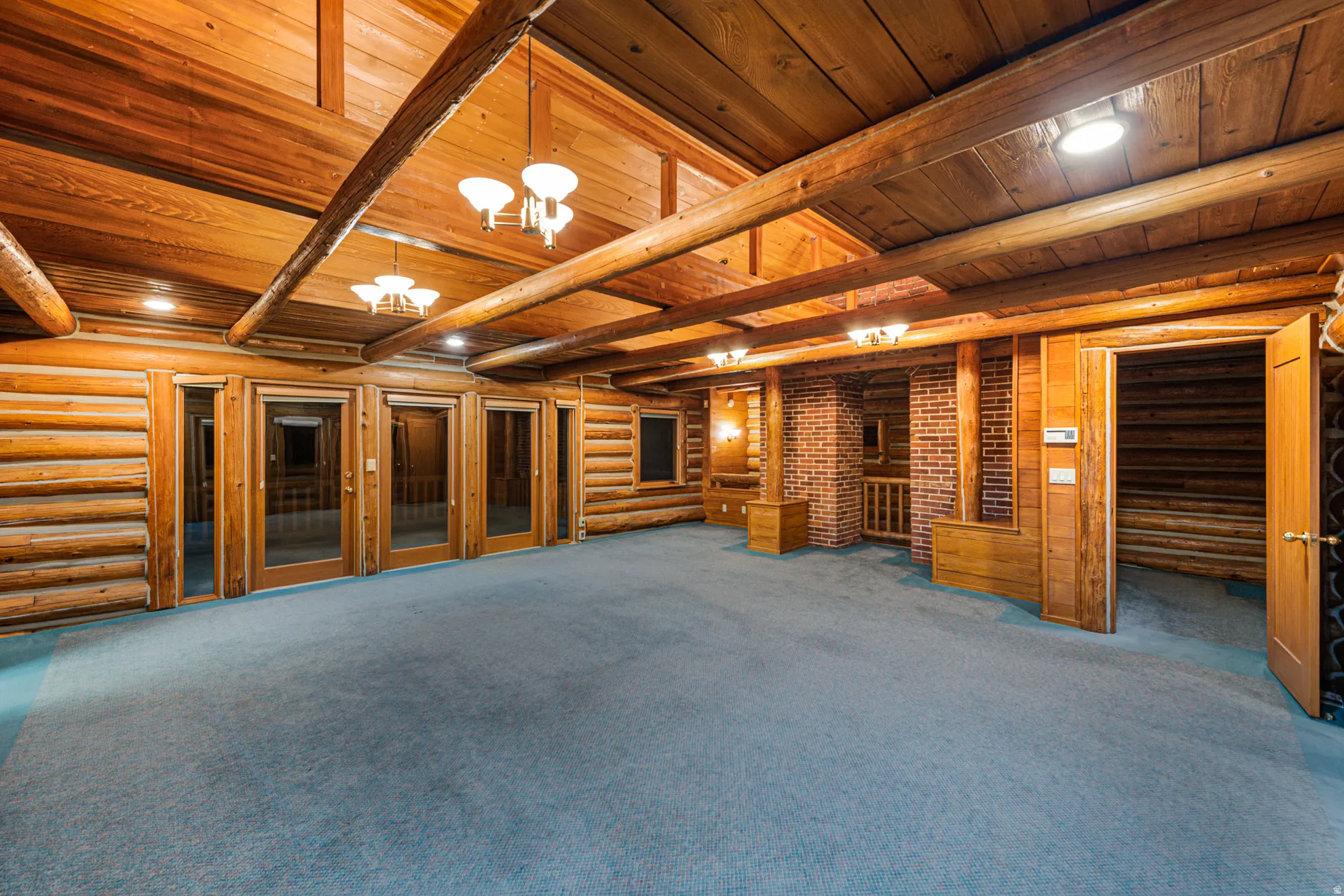 Exposed wood beam ceiling, wood plank walls, recessed lighting, chandelier lighting, and an interior brick-clad architectural element