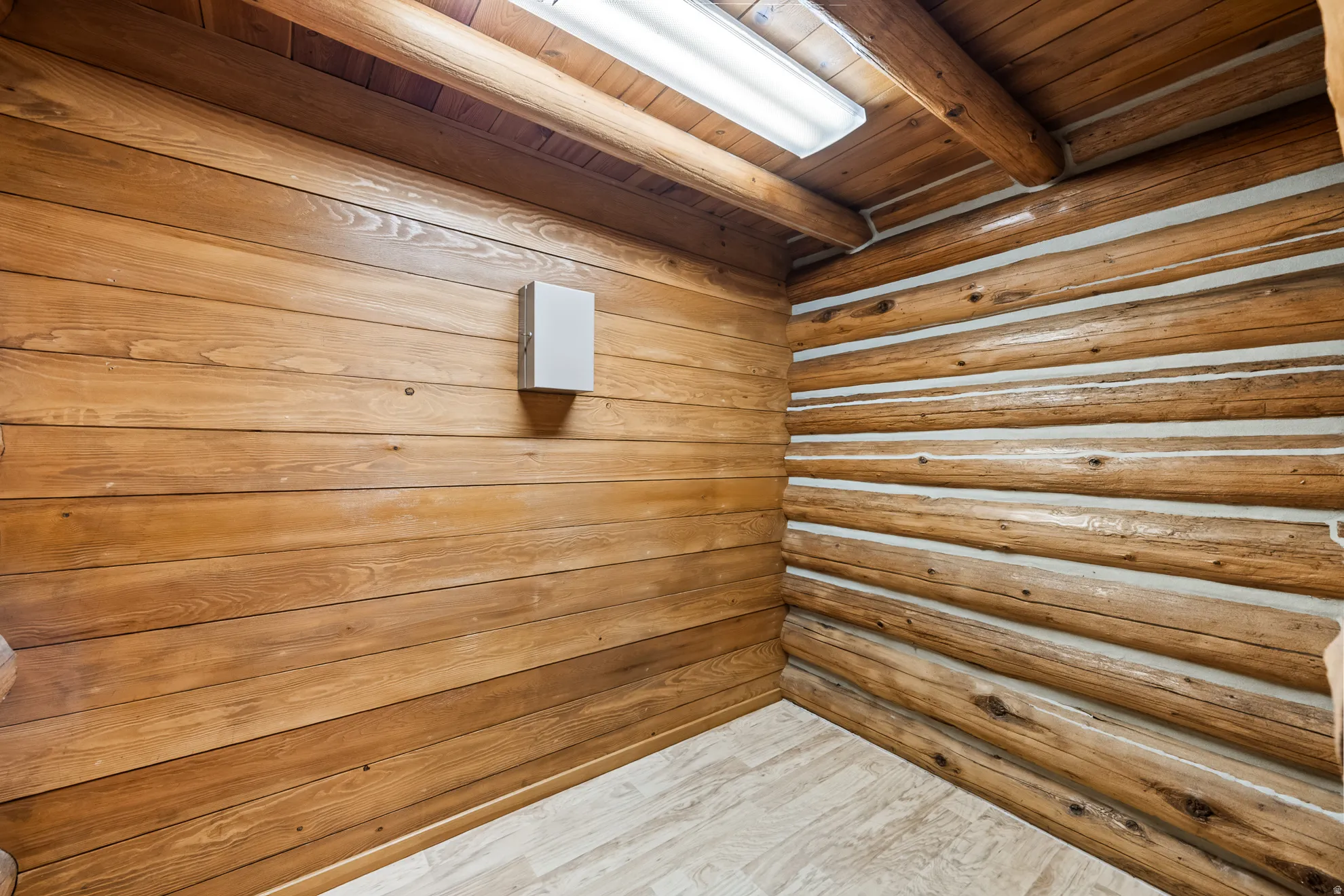 Rustic interior space featuring log and plank wood walls, a wood-finish ceiling with exposed beams, and a fluorescent ceiling light fixture