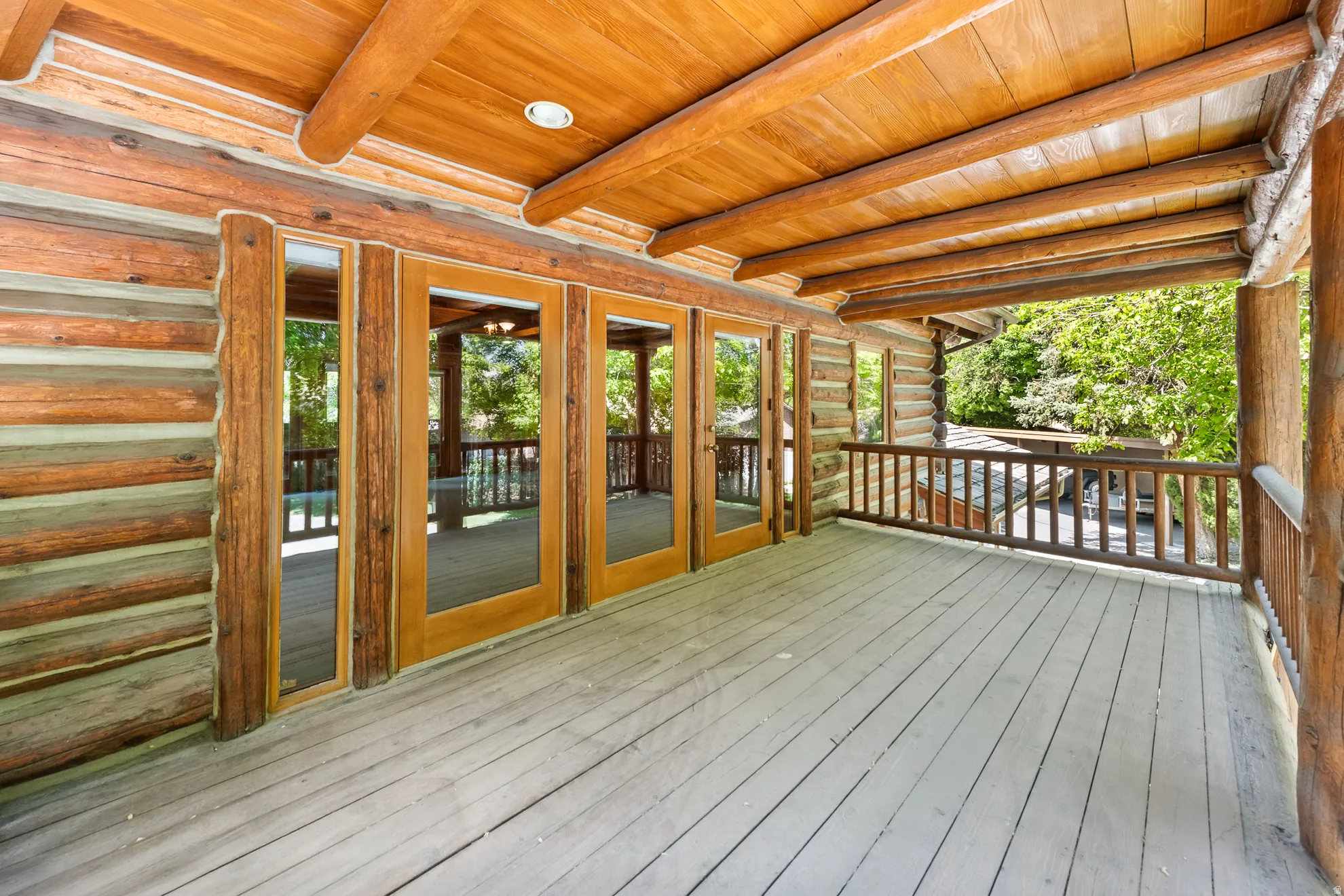 Spacious deck with natural wood railing, log beam construction, and multiple glass-paneled doors
