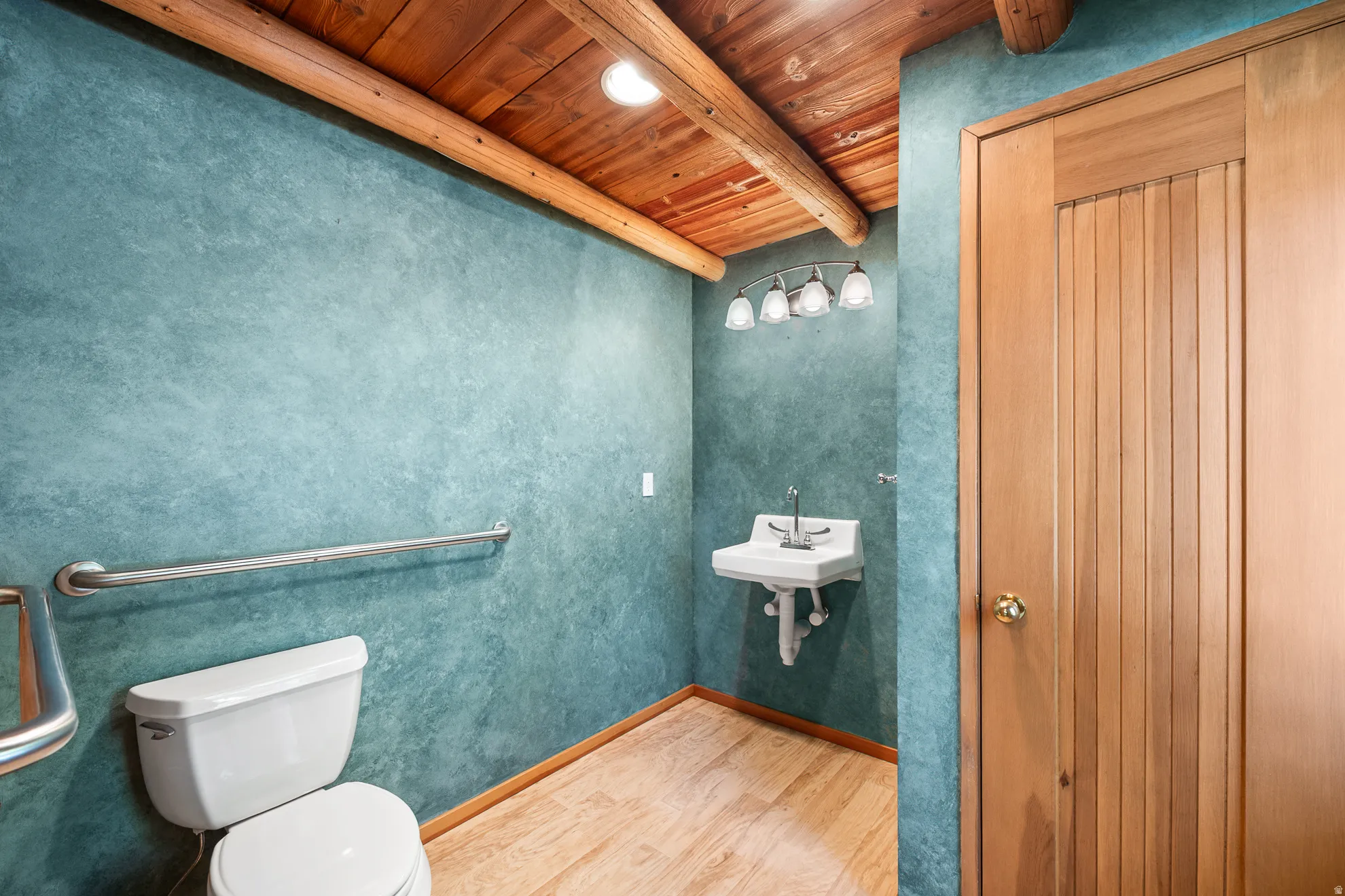 Bathroom featuring a wall-mounted sink, ceramic toilet, and wood-finish flooring