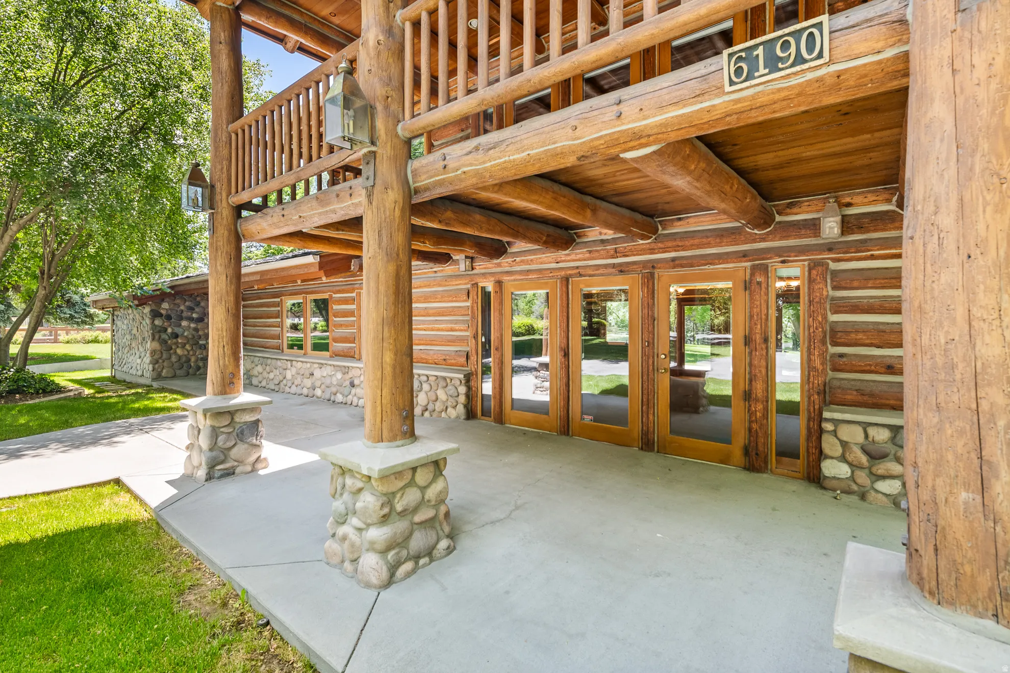 Log cabin exterior featuring a covered concrete patio, stone column bases, timber pillars, and multiple glass-paned doors