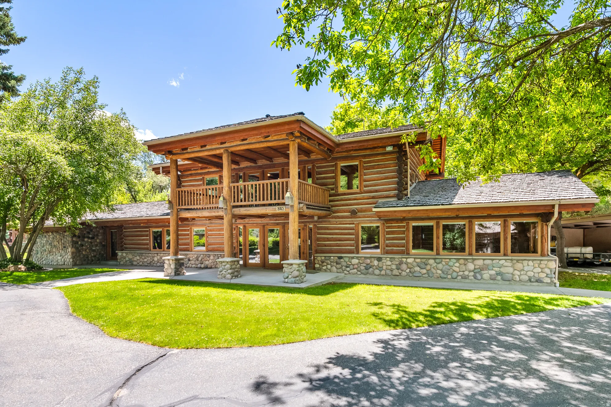 Log cabin exterior featuring a multi-level design, a stone facade foundation, and a second-story balcony