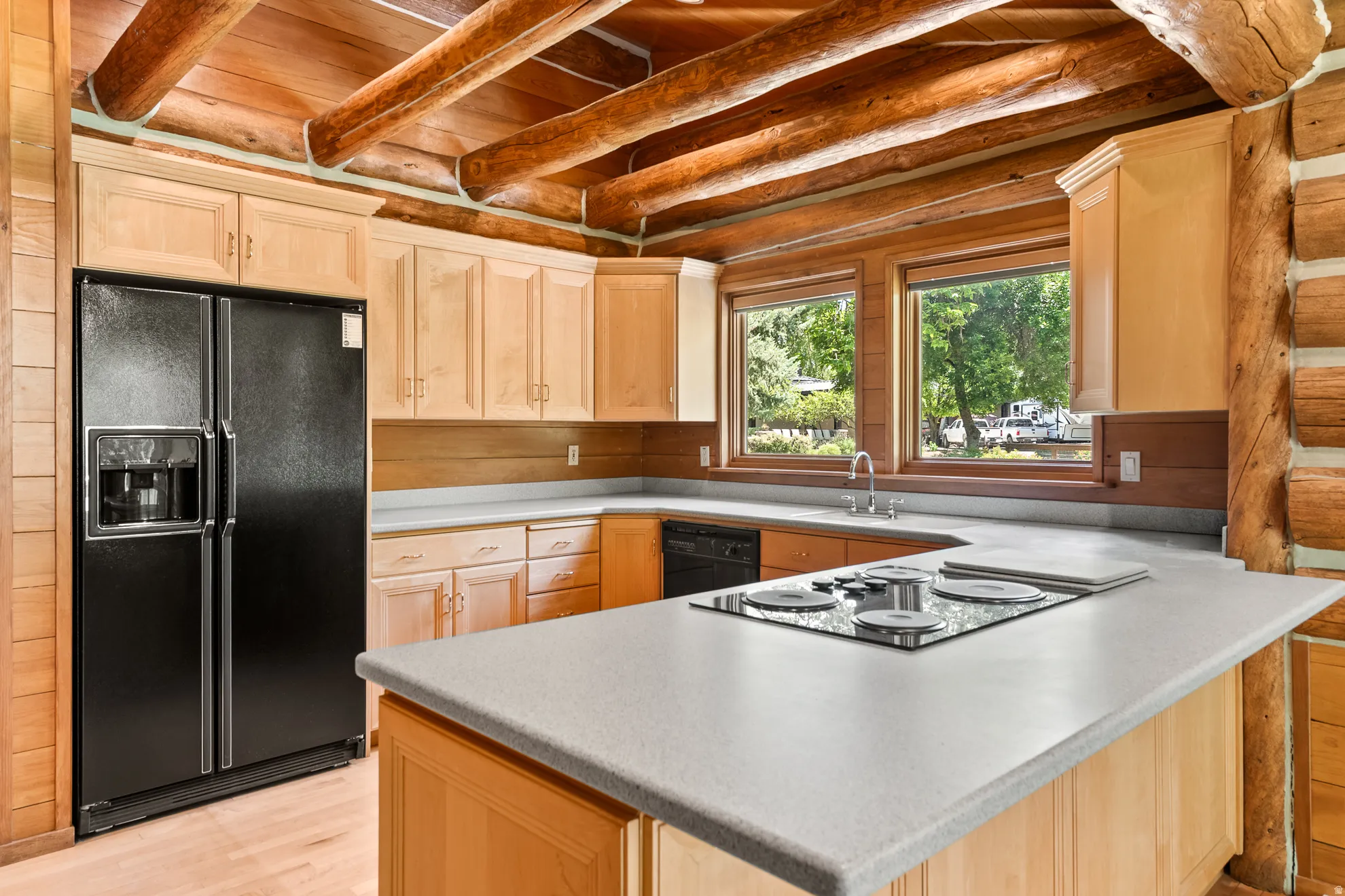 Kitchen featuring log walls, exposed wood beams, wood-finish flooring, light wood cabinetry, and solid surface countertops