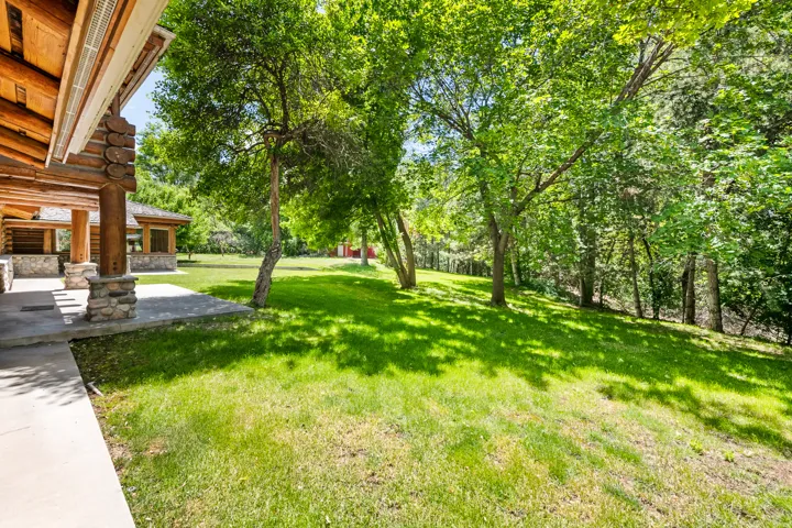 Expansive green lawn surrounded by mature trees, featuring a concrete patio with natural stone pillars and exposed log beams