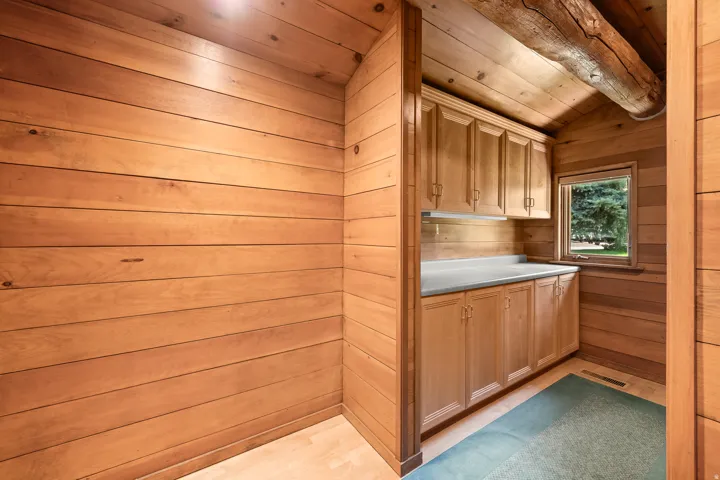 Wood-paneled room featuring custom wood cabinetry with a light-toned countertop, a window with exterior views, and an exposed wood beam ceiling