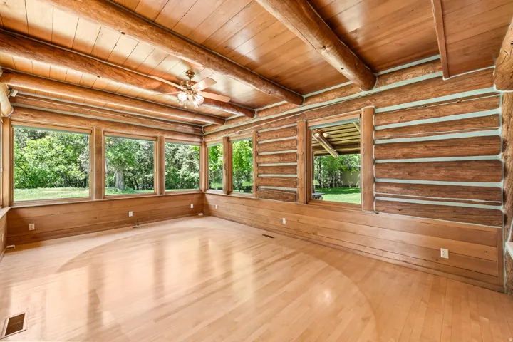 Sun-filled room featuring exposed log walls, wood-finish flooring, a wood plank ceiling with exposed beams, and multiple picture windows