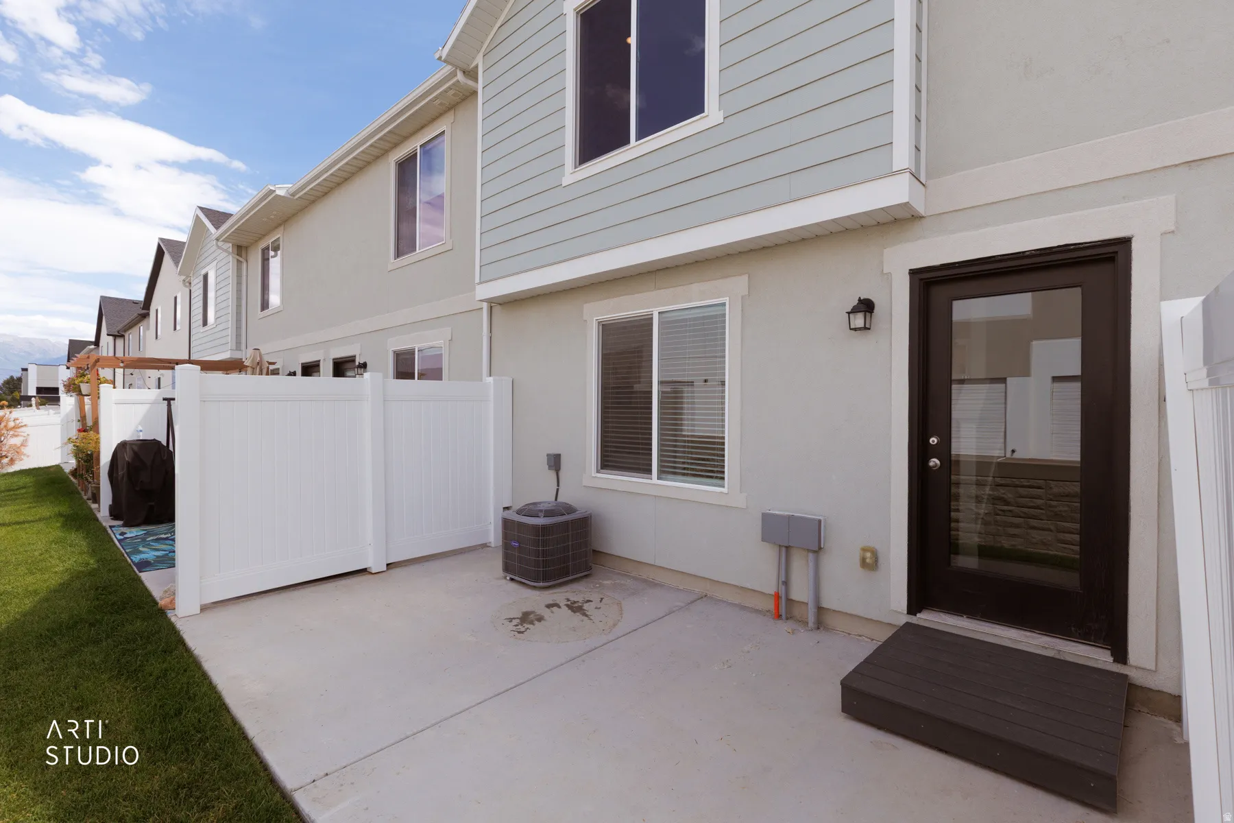 Paved outdoor patio with a privacy fence, exterior lighting, a dark-framed glass door, and a wooden step platform