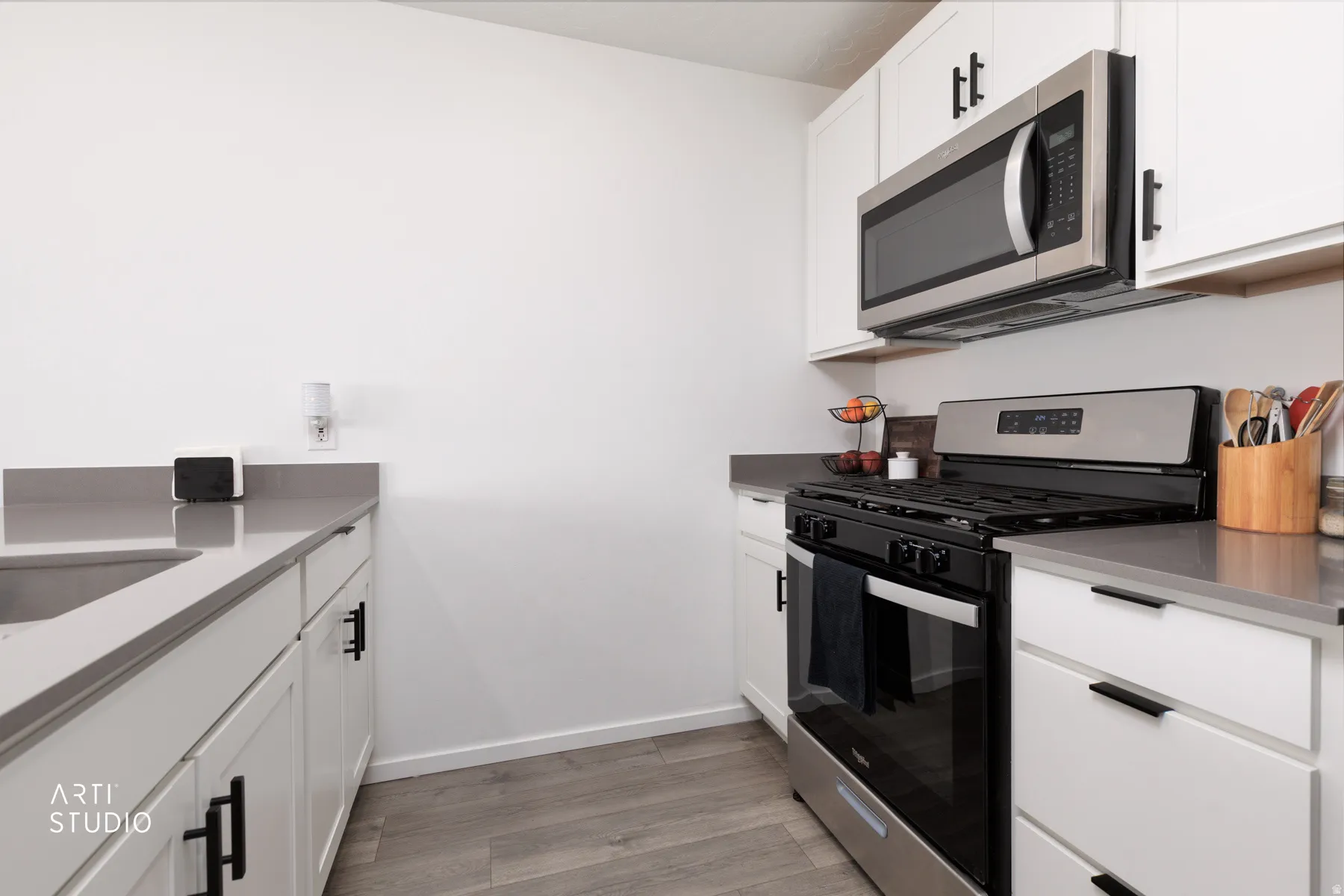 White cabinetry with black hardware, stainless steel microwave, stainless steel range, gray countertops, and wood-finish flooring