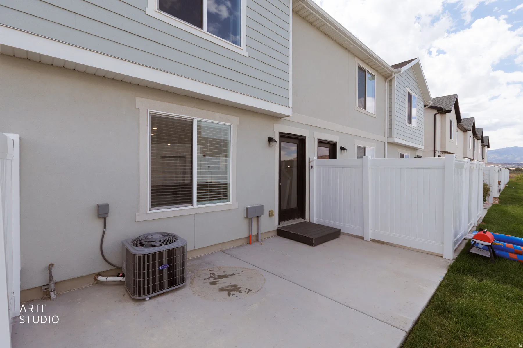 Concrete patio, white vinyl fencing, stucco exterior, rear entry door, and a grass lawn