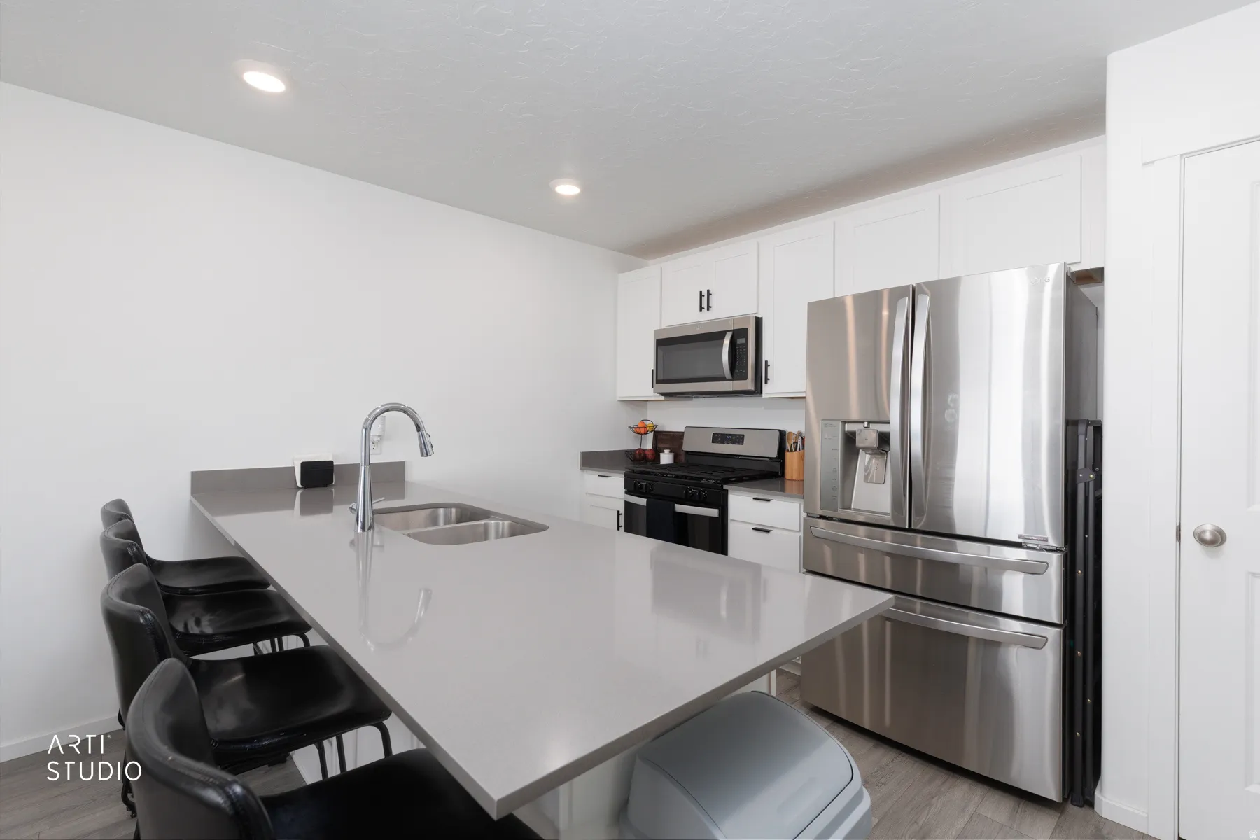 Kitchen with stainless steel appliances, white cabinetry, recessed lighting, and a large island featuring an undermount sink and gooseneck faucet