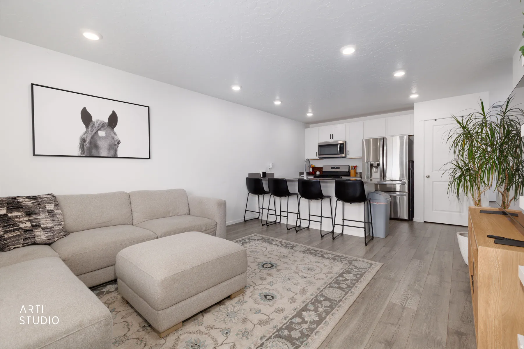 Recessed lighting, wood-finish flooring, white cabinetry, stainless steel appliances, and a kitchen island with bar seating