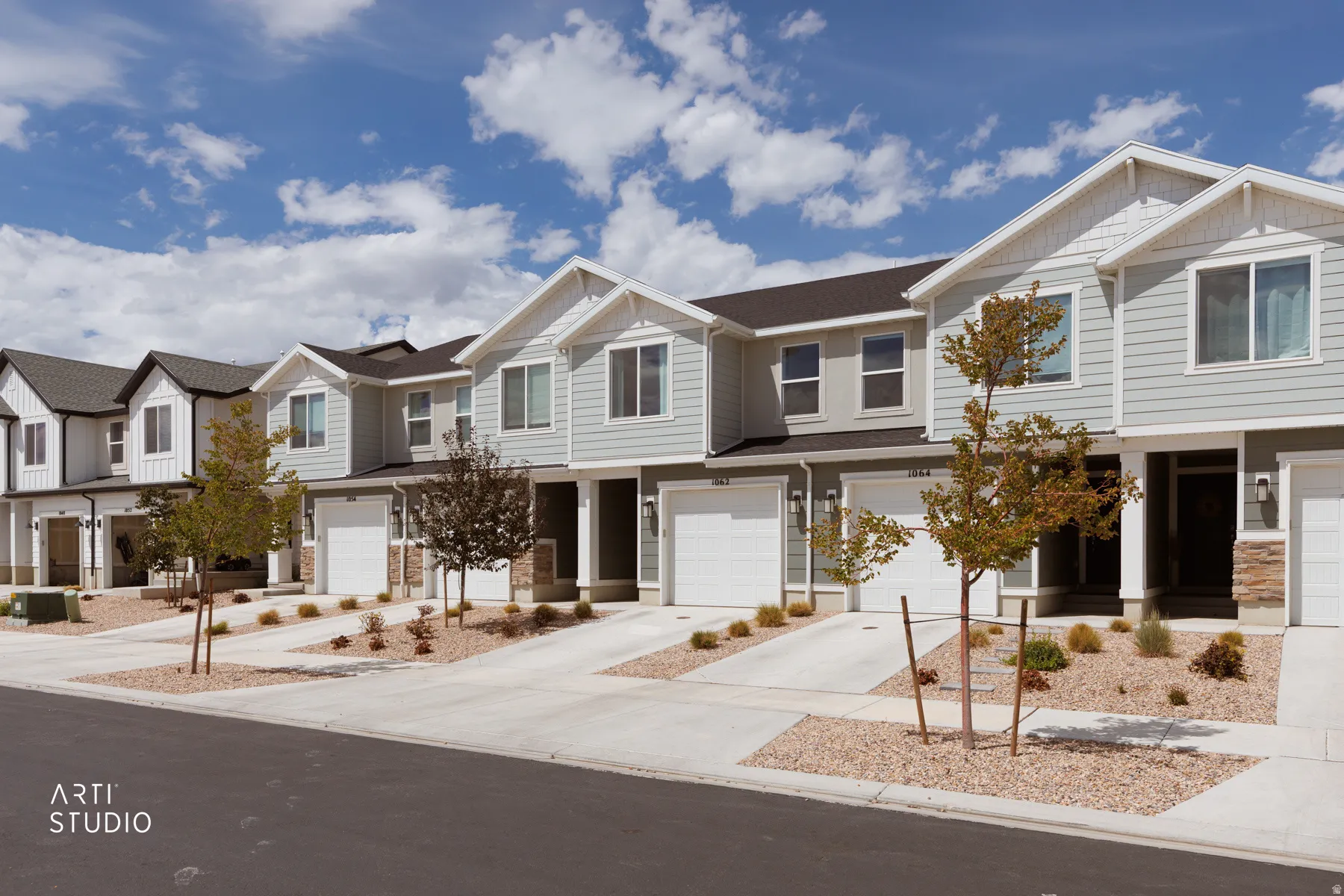 Modern townhome exteriors featuring light gray siding, white trim, attached garages, and stone accents