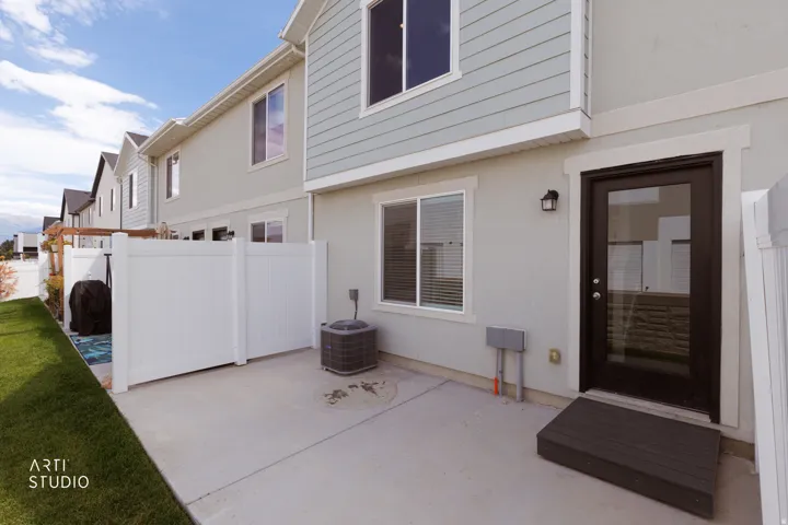 Paved outdoor patio with a privacy fence, exterior lighting, a dark-framed glass door, and a wooden step platform