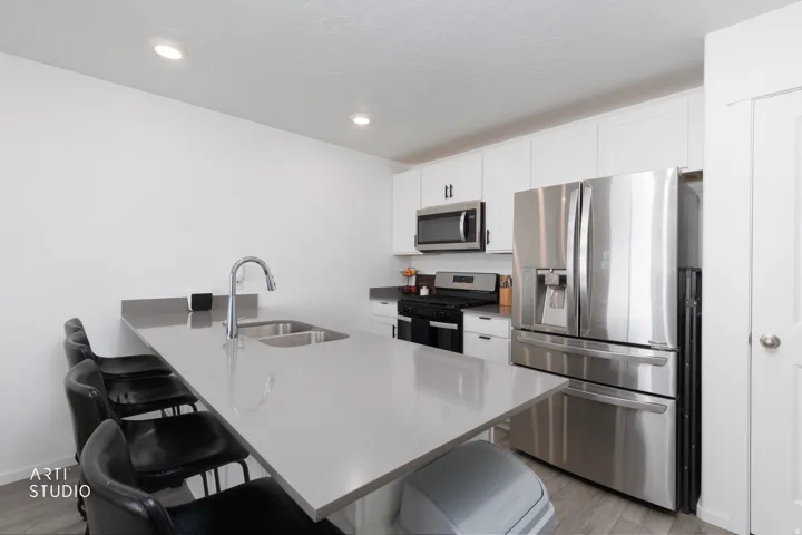 Kitchen with stainless steel appliances, white cabinetry, recessed lighting, and a large island featuring an undermount sink and gooseneck faucet