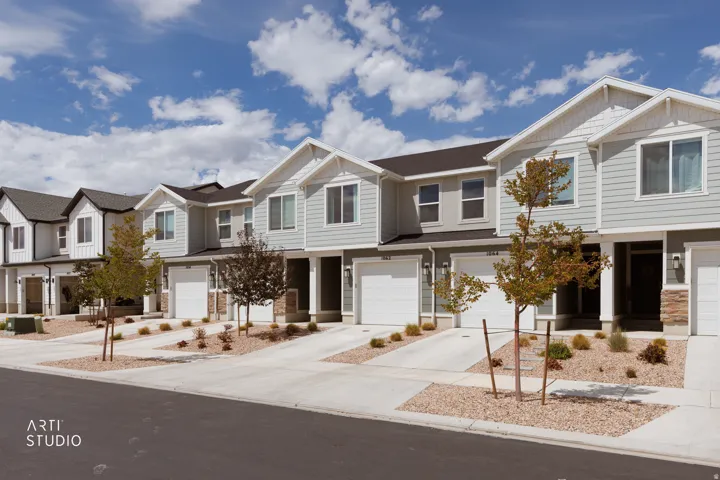 Modern townhome exteriors featuring light gray siding, white trim, attached garages, and stone accents