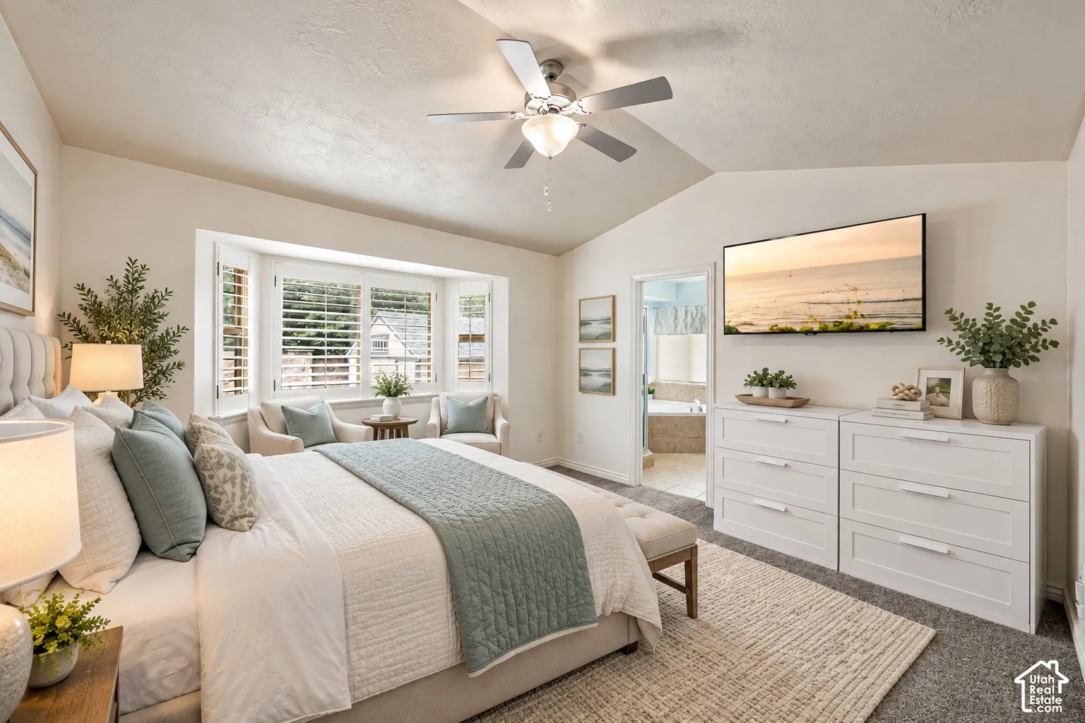 Vaulted ceiling with a central brushed-nickel ceiling fan, bay window featuring plantation shutters, and wall-to-wall carpeting