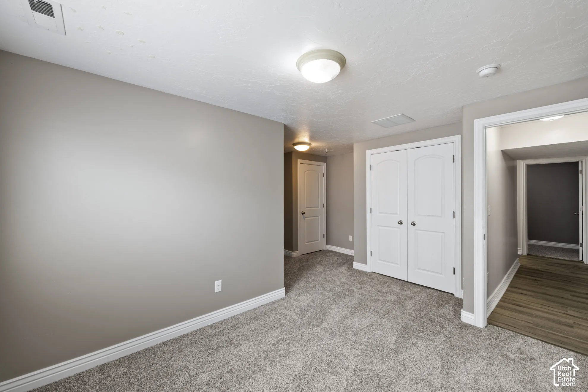 Neutral gray wall paint, textured carpet, white bi-fold closet doors, recessed ceiling light fixtures, wood-finish flooring