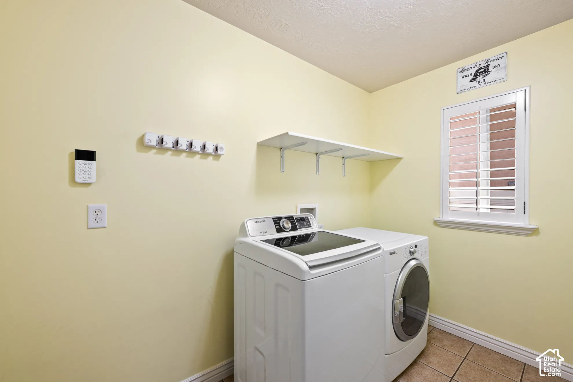 Laundry area featuring a window with plantation shutters, tile flooring, and a wall-mounted shelf
