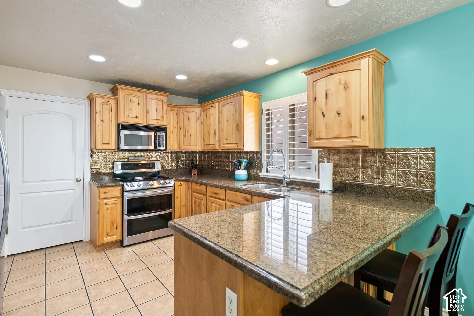 Kitchen featuring extensive wood cabinetry, stainless steel appliances, a bar-height counter, tile flooring, and recessed ceiling lighting