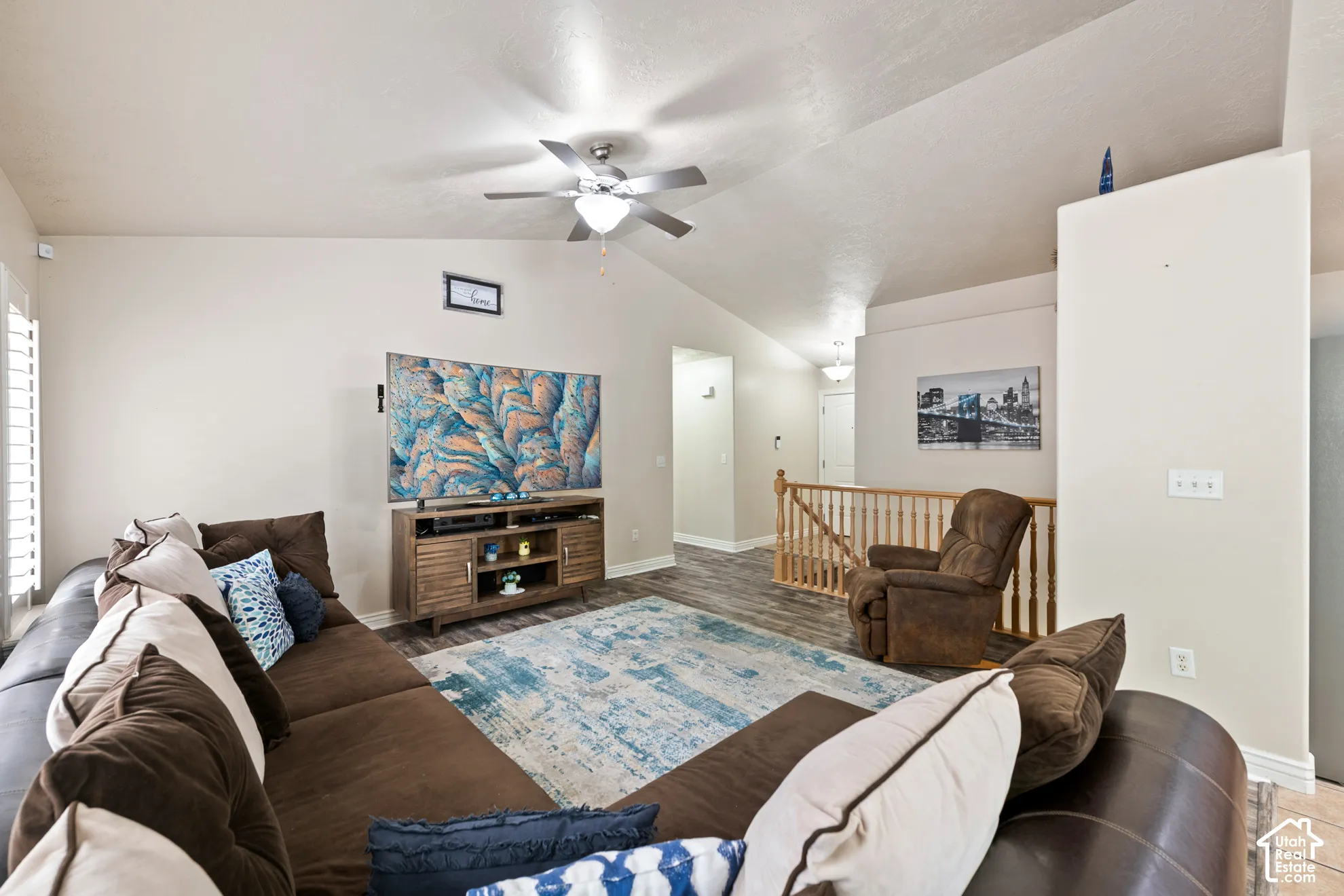 Spacious living area featuring vaulted ceilings, wood-finish flooring, plantation shutters, and a ceiling fan