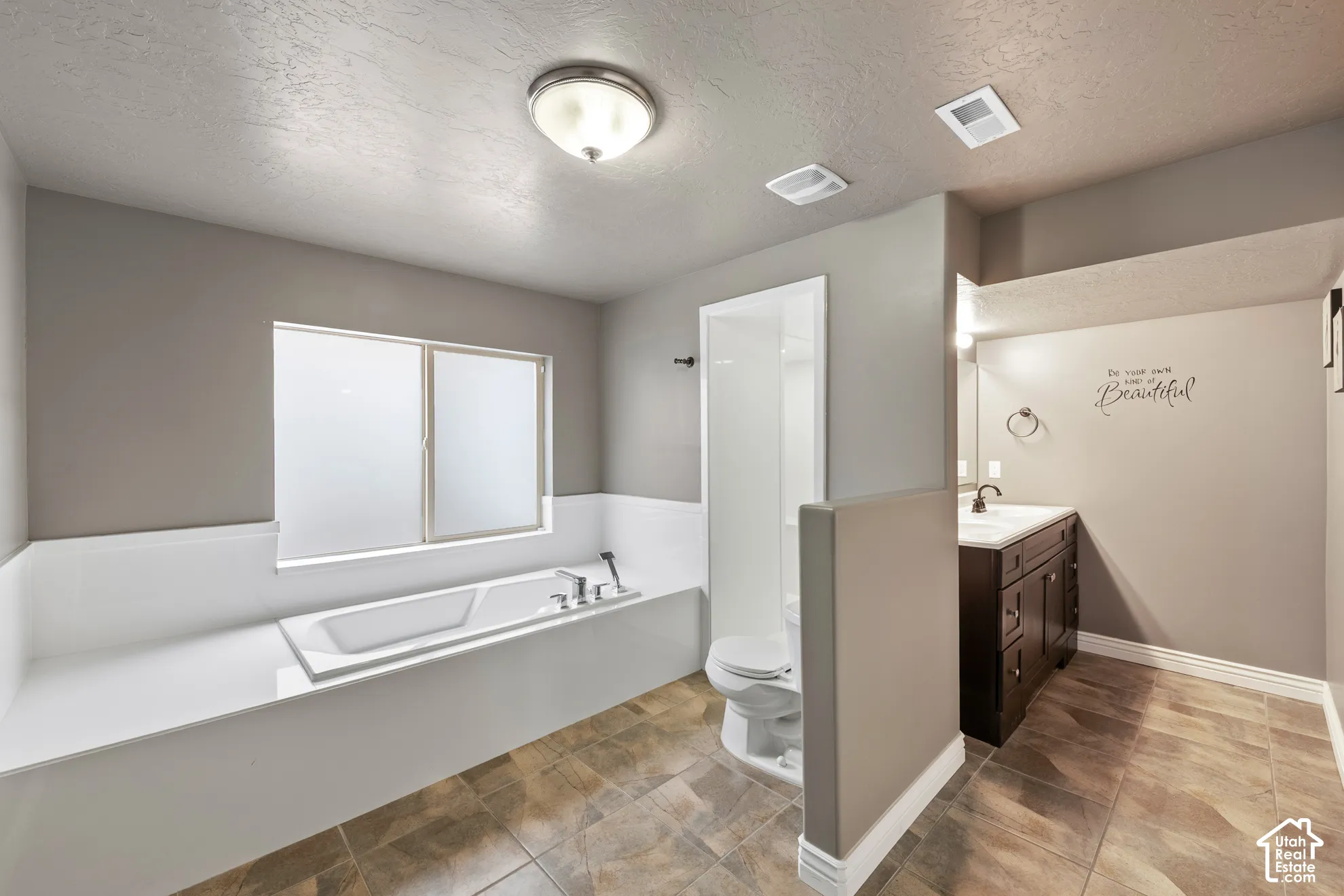 Soaking tub with a frosted window, separate shower enclosure, single vanity with dark wood cabinetry, and neutral-toned floor tiling