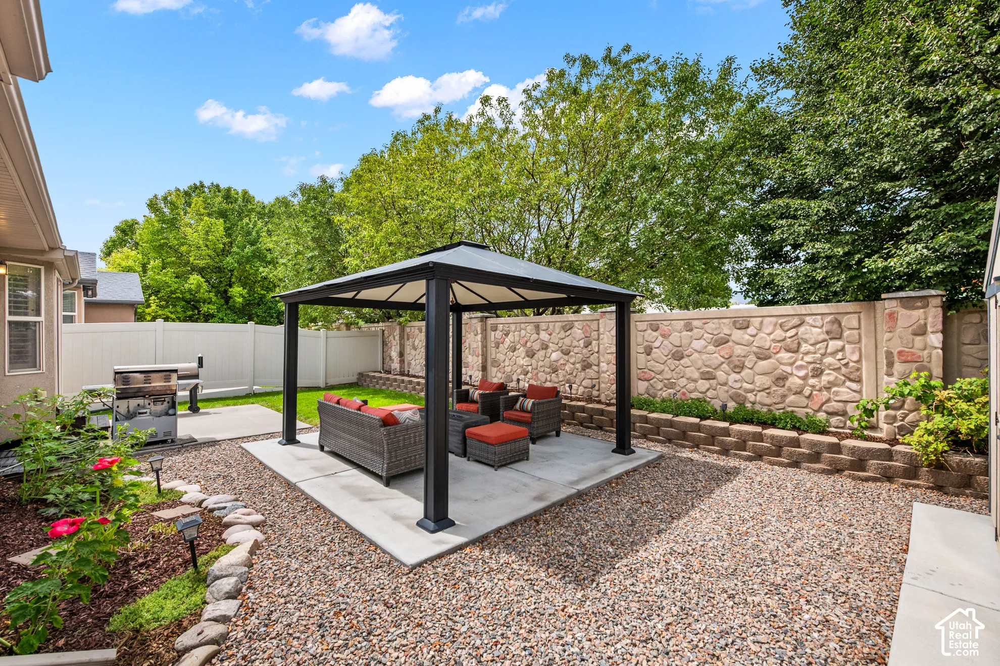 Expansive backyard featuring a stone-clad privacy wall, a covered gazebo on a concrete pad, a manicured lawn area, and gravel landscaping
