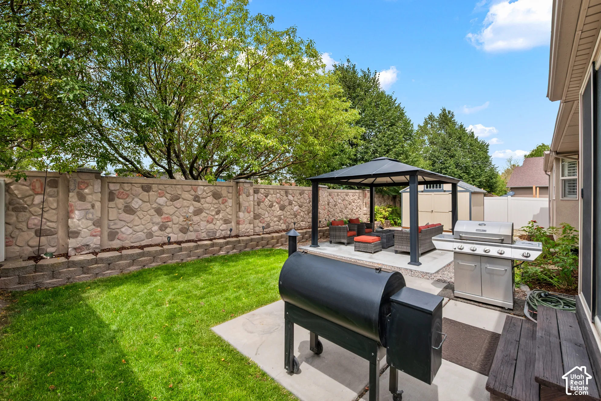 Private backyard featuring a stone and concrete privacy wall, concrete patio, and a covered gazebo structure