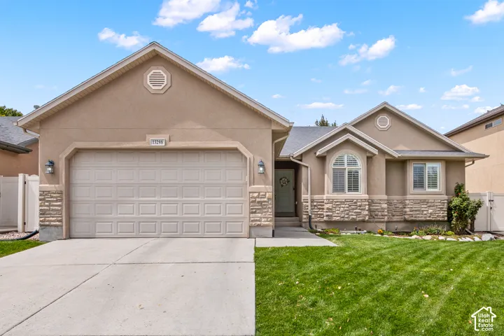 Stucco exterior with stone accents, attached two-car garage, concrete driveway, and front lawn