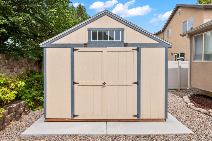 Gable-roof storage shed with a transom window, double doors, and a concrete pad base