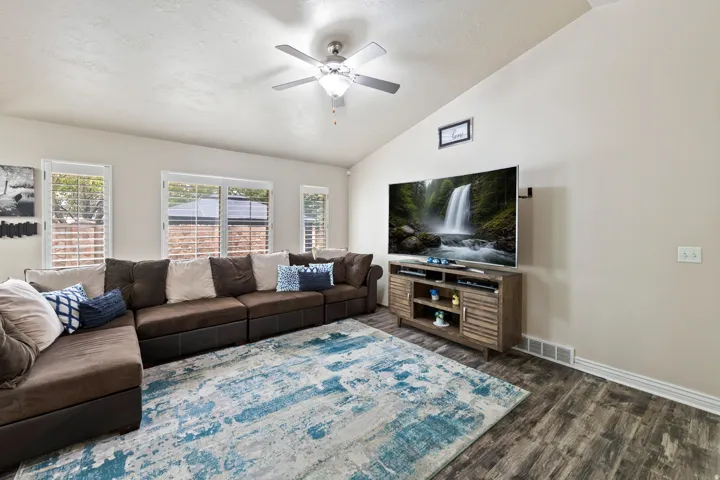 Vaulted ceiling with an attached ceiling fan, wood-finish flooring, and multiple windows with plantation shutters