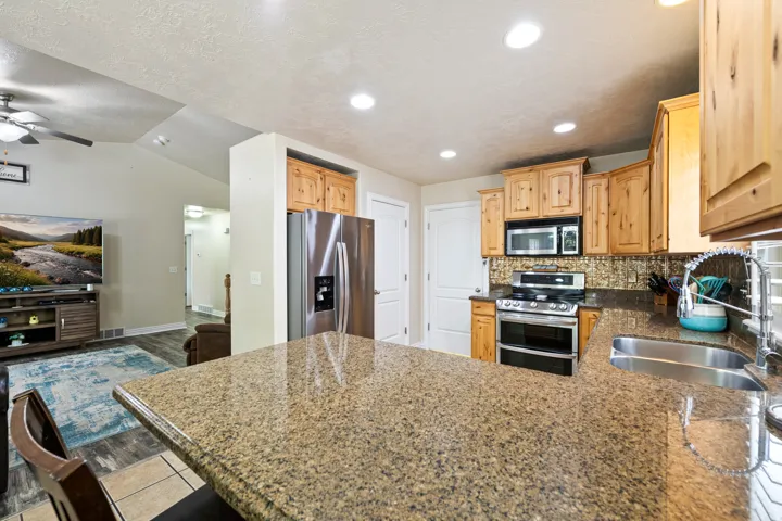 Kitchen featuring a double basin stainless steel sink, stainless steel appliances, wood-finish cabinetry, and a textured backsplash, with a stone-finish countertop extending into a breakfast bar