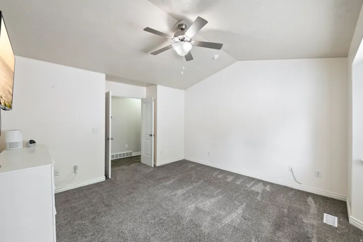 Vaulted ceiling, ceiling fan with integrated lighting, gray carpeting, and white walls