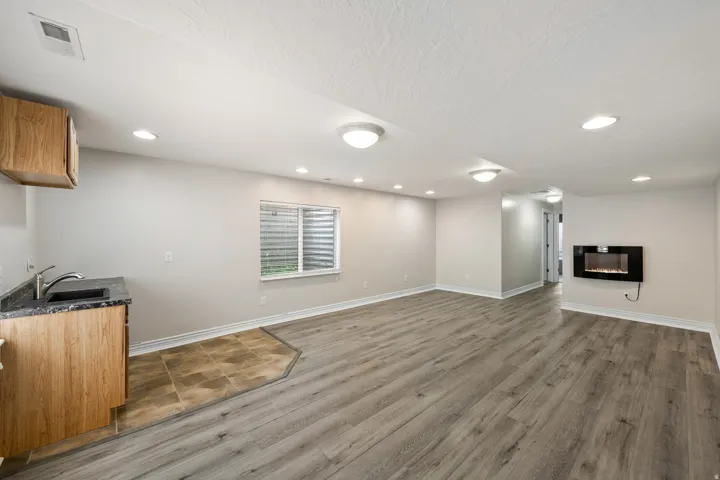 Spacious room featuring wood-finish flooring, recessed lighting, a built-in electric fireplace, and a kitchenette with wood cabinetry, a sink, and a dark countertop