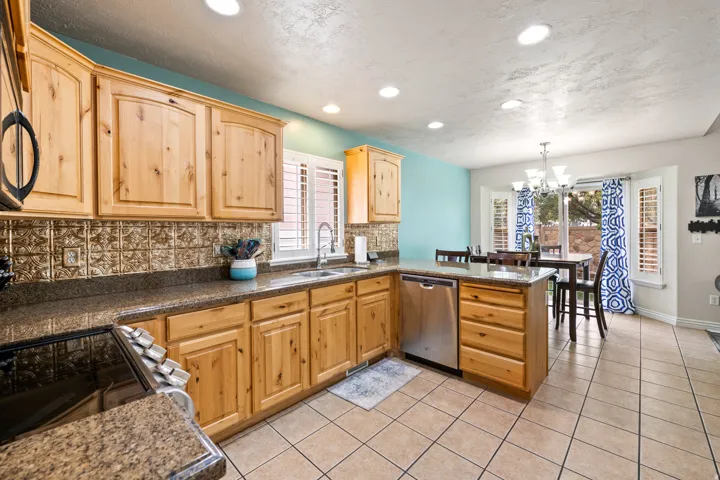 Warm wood cabinetry, integrated stainless steel dishwasher, brown speckled countertops, tile backsplash, and recessed lighting