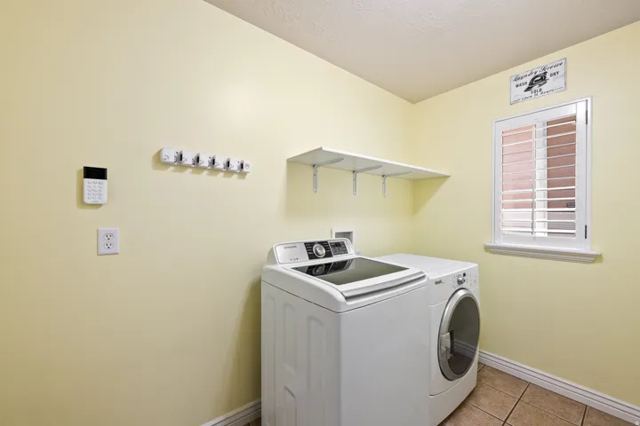 Laundry area featuring a window with plantation shutters, tile flooring, and a wall-mounted shelf